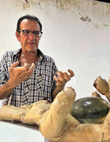 Fotografía de portada del escultor Jorge Alfaro posando junto a su obra en el Fortín Álvarez. El artista posa con su mano real como  está en la escultura con forma de mano humana texturizada con piel de cordero y cicatrices, montada sobre un cubo.