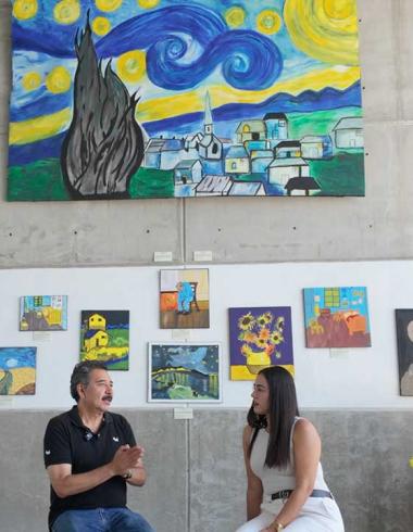 Entrevista a la Maestra Iliana Fuentes en la Sala de Exposiciones del Fuerte de San Diego, rodeada de pinturas de girasoles y réplicas de obras de Vincent van Gogh hechas por estudiantes.