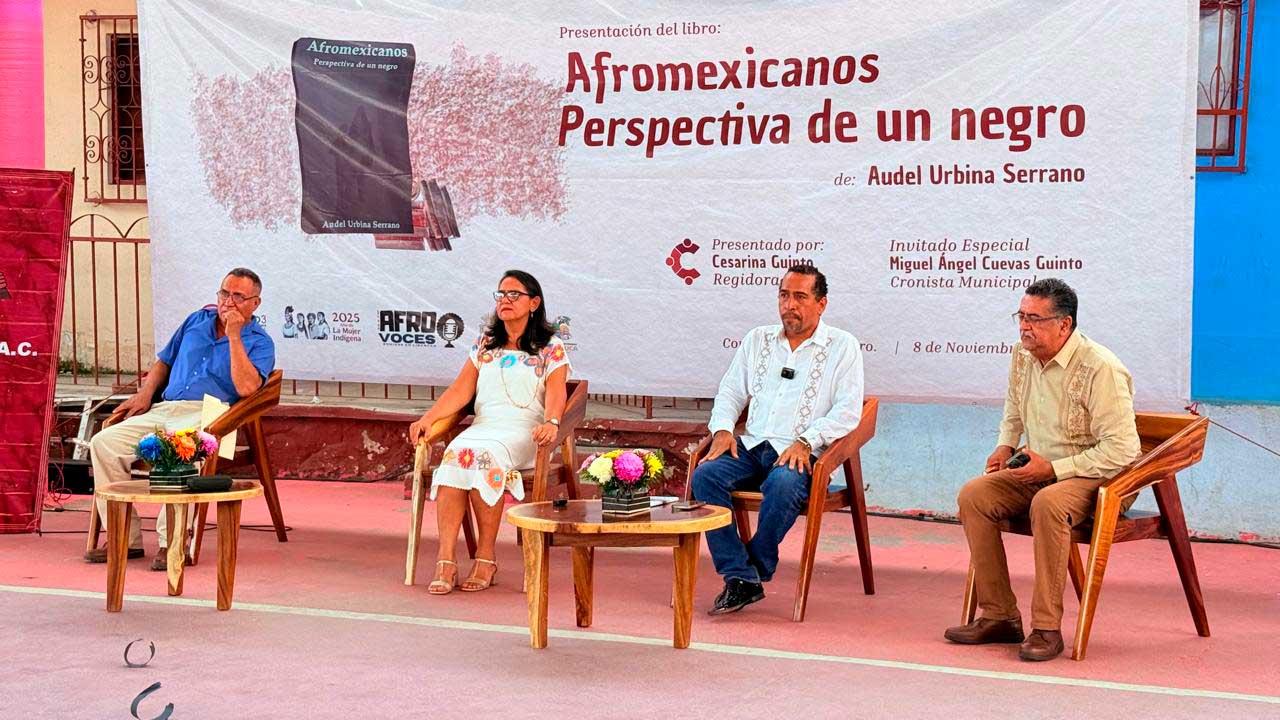 Audel Urbina Serrano presenta su libro "Afromexicanos, perspectiva de un negro" en Coyuca de Benítez, acompañado por la regidora Cesarina Quinto, el cronista Miguel Ángel Cuevas Quinto y otros invitados, frente al banner oficial del evento.