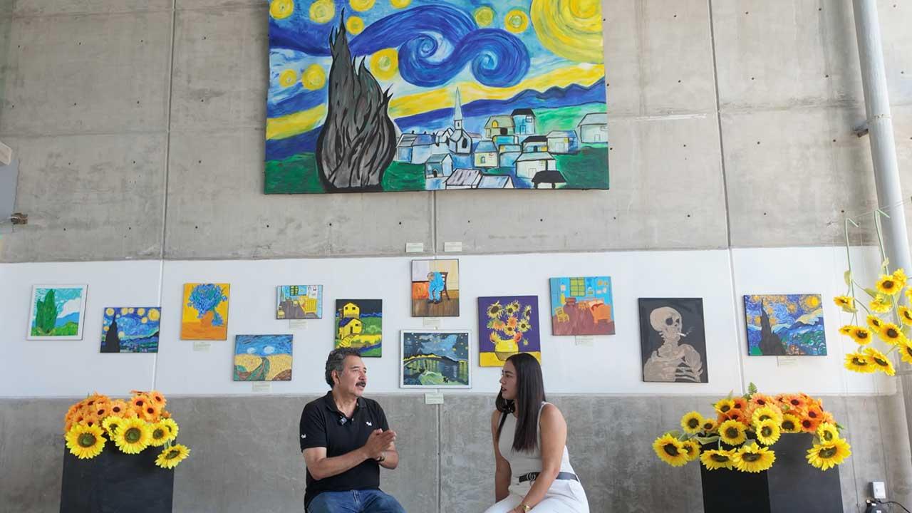 Entrevista a la Maestra Iliana Fuentes en la Sala de Exposiciones del Fuerte de San Diego, rodeada de pinturas de girasoles y réplicas de obras de Vincent van Gogh hechas por estudiantes.