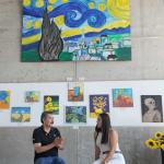Entrevista a la Maestra Iliana Fuentes en la Sala de Exposiciones del Fuerte de San Diego, rodeada de pinturas de girasoles y réplicas de obras de Vincent van Gogh hechas por estudiantes.