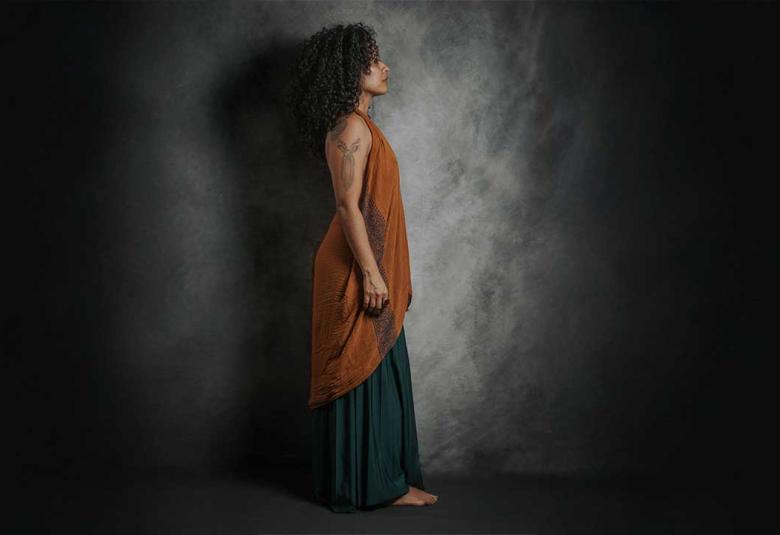 Miriam Teresa de perfil, de cuerpo completo, observa a la lejanía en una atmósfera oscura y ocre.