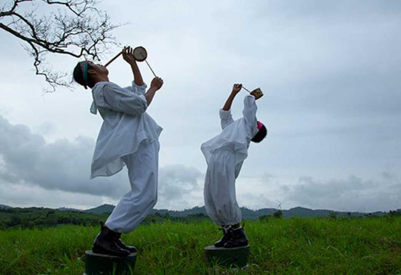 Danzante volador adulto y niño de Papantla ejecutando la música ritual - hombre tocando tambor tradicional y niño soplando flauta de carrizo durante la ceremonia de los Voladores de Papantla al aire libre.