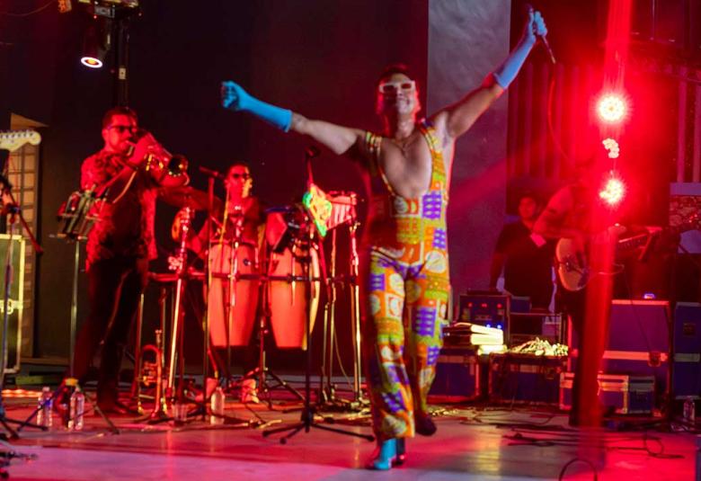 Erik Castrejón se encuentra sobre el escenario del Auditorio del Parque Papagayo de Acapulco con los brazos levantados y un micrófono en una de sus manos, mientras los músicos de su banda permanecen detrás de él durante el concierto homenaje a Juan Gabriel Amor eterno, rolitas de Juanga para mamá.