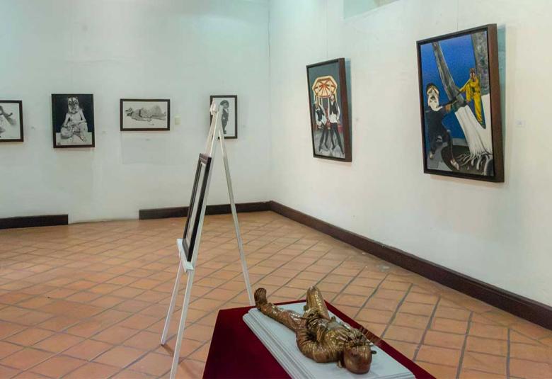 Vista panorámica de la exposición "Orgullo de mis raíces: Copanatoyac" en una sala del Museo Universitario José Juárez. Las pinturas de Miguel Altamirano Velázquez se exhiben en los muros junto con cédulas informativas, mostrando escenas inspiradas en la danza del Tekuanimej y las tradiciones de Copanatoyac, Guerrero.