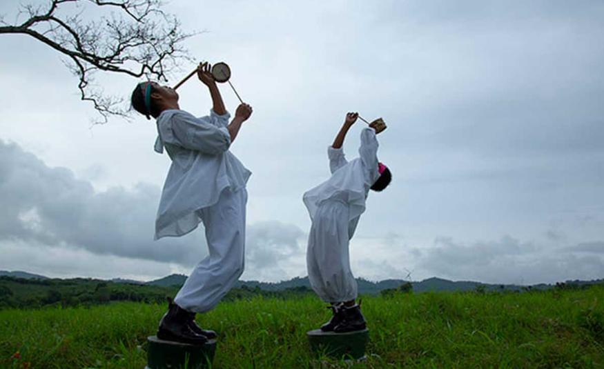 Danzante volador adulto y niño de Papantla ejecutando la música ritual - hombre tocando tambor tradicional y niño soplando flauta de carrizo durante la ceremonia de los Voladores de Papantla al aire libre.