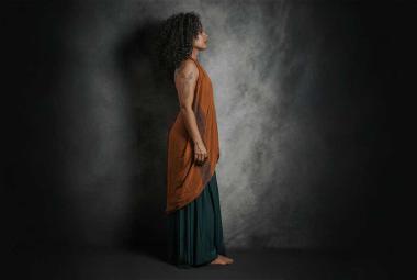 Miriam Teresa de perfil, de cuerpo completo, observa a la lejanía en una atmósfera oscura y ocre.