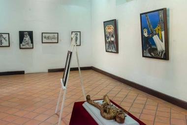 Vista panorámica de la exposición "Orgullo de mis raíces: Copanatoyac" en una sala del Museo Universitario José Juárez. Las pinturas de Miguel Altamirano Velázquez se exhiben en los muros junto con cédulas informativas, mostrando escenas inspiradas en la danza del Tekuanimej y las tradiciones de Copanatoyac, Guerrero.