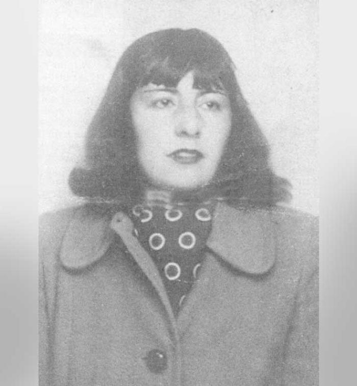 Fotografía en blanco y negro de María Luisa Bombal, tomada de su pasaporte. Ella es una mujer joven con cabello oscuro hasta los hombros, peinado en un bob con flequillo. Mira directamente a la cámara con una expresión seria. Viste un abrigo oscuro con solapas anchas y debajo, un pañuelo de cuello con un patrón de lunares o círculos blancos. La foto tiene un aspecto vintage y está enmarcada por bordes grises y borrosos.